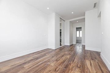 Spacious empty bedroom with dark wooden floorboards, fitted mirrored wardrobes and access to an en-suite toilet