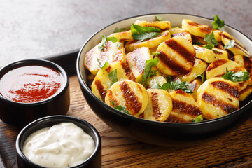 Grilled potatoes with stripes and two sauces close-up on a wooden board on the table. horizontal