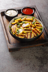 Sliced Of Village Style BBQ Potatoes with sauces served on a wooden board on the table closeup. Vertical