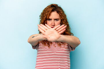 Young ginger caucasian woman isolated on blue background doing a denial gesture