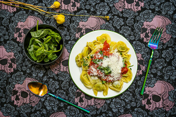 Italian pasta dish with a lot of basil, tomato sauce and grated cheese on a skull tablecloth