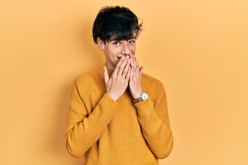 Handsome hipster young man wearing casual yellow sweater laughing and embarrassed giggle covering...