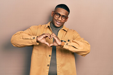 Young black man wearing casual clothes and glasses smiling in love showing heart symbol and shape...