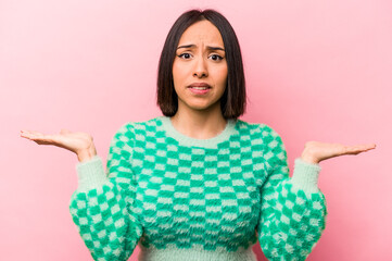 Young hispanic woman isolated on pink background confused and doubtful shrugging shoulders to hold...