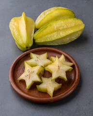 Starfruits with slices on a plate over stone background