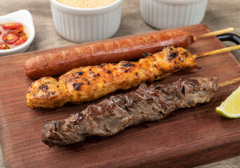 Meat, chicken and pork sausage skewers over wooden board with farofa, lemon and pepper
