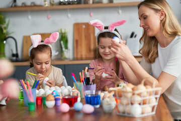 Cheerful caucasian mother and daughters decorates easter eggs in domestic kitchen
