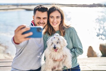 Man and woman holding dog making selfie by the smartphone at seaside