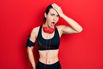 Young hispanic girl wearing gym clothes and using headphones surprised with hand on head for mistake, remember error. forgot, bad memory concept.