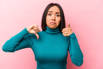 Young hispanic woman isolated on pink background showing thumbs up and thumbs down, difficult choose concept