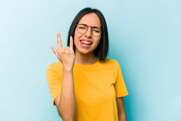 Young hispanic woman isolated on blue background showing rock gesture with fingers