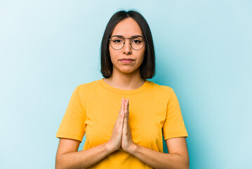 Young hispanic woman isolated on blue background praying, showing devotion, religious person...