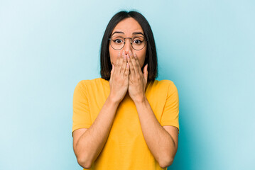 Young hispanic woman isolated on blue background shocked, covering mouth with hands, anxious to discover something new.