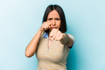 Young hispanic woman isolated on blue background throwing a punch, anger, fighting due to an argument, boxing.