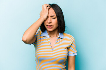 Young hispanic woman isolated on blue background forgetting something, slapping forehead with palm...