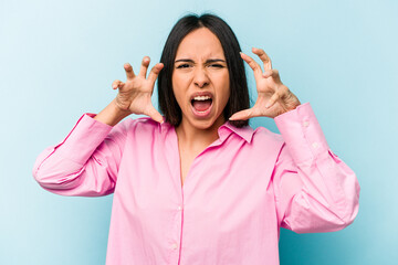 Young hispanic woman isolated on blue background upset screaming with tense hands.
