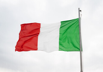 Italian flag flying in the wind against a cloudy sky.