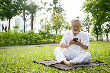 An elderly man using smartphone searching yoga lession and enjoys a break from hard exercise. Health insurance and relaxation after retirement.