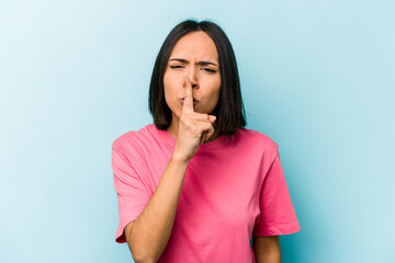 Young hispanic woman isolated on blue background keeping a secret or asking for silence.