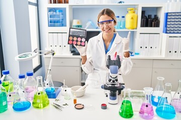 Young blonde woman working at scientist laboratory with make up smiling with an idea or question pointing finger with happy face, number one