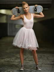 Dainty yet daring. A young ballerina holding a skateboard while wearing a tutu and sneakers.