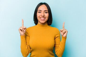 Young hispanic woman isolated on blue background indicates with both fore fingers up showing a...