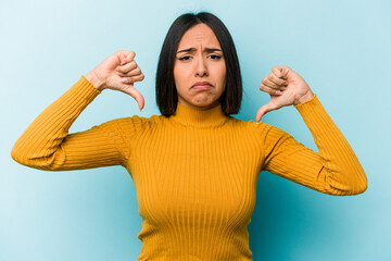 Young hispanic woman isolated on blue background showing a dislike gesture, thumbs down....