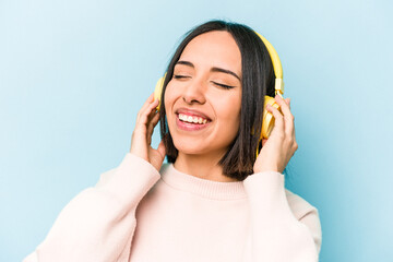 Young hispanic woman listening to music isolated on blue background