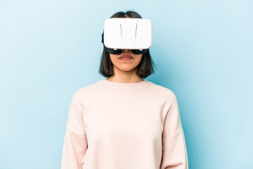 Young hispanic woman wearing a virtual glasses isolated on blue background