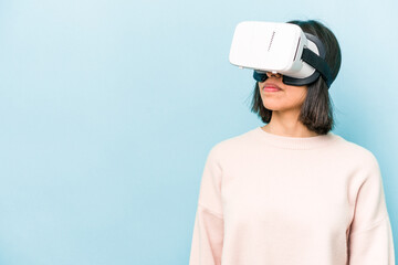Young hispanic woman wearing a virtual glasses isolated on blue background