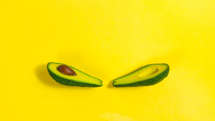 Two halves of a ripe avocado with a stone in the middle on a yellow background close-up.
