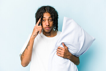 Young African American man holding a pillow isolated on blue background pointing temple with finger, thinking, focused on a task.