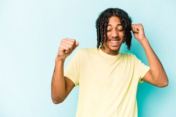 Young African American man isolated on blue background raising fist after a victory, winner concept.