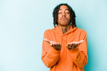 Young African American man isolated on blue background folding lips and holding palms to send air kiss.