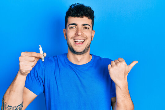 Young hispanic man holding spark plug pointing thumb up to the side smiling happy with open mouth