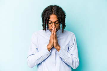 Young African American man isolated on blue background praying, showing devotion, religious person looking for divine inspiration.