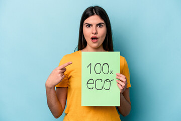 Young caucasian woman holding 100% eco placard isolated on blue background pointing to the side