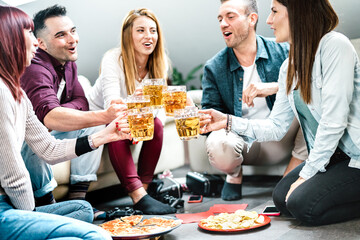 Young student friends toasting beer at home party after college time - Life style concept with millenial roommates enjoying drinks together and having fun eating at shared apartment - Bright filter