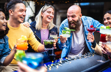 Trendy young people toasting multicolored fresh drinks at fashion bar - Gen z friends having fun...