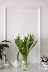 A bouquet of white tulips stands in a vase on a white table