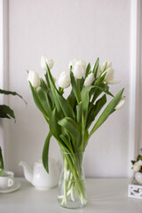 A bouquet of white tulips stands in a vase on a white table