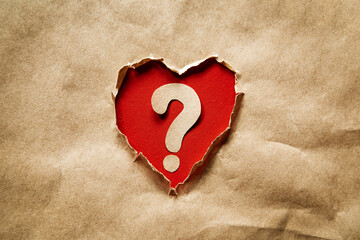 Heart shaped hole in kraft paper. Inside a question mark on a red background.