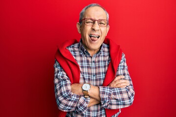 Handsome senior man with grey hair wearing casual clothes and glasses sticking tongue out happy with funny expression.