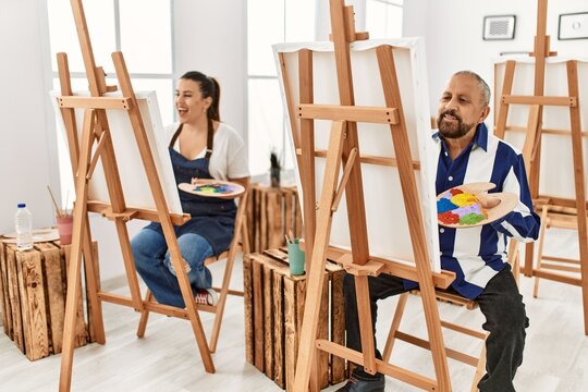 Young artist woman and senior painter man at art studio classroom painting on canvas with brush and oil painting