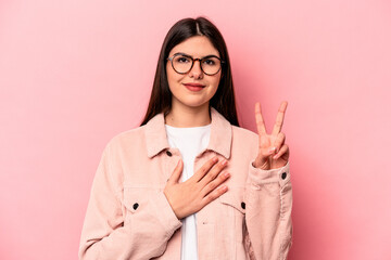 Young caucasian woman isolated on pink background taking an oath, putting hand on chest.