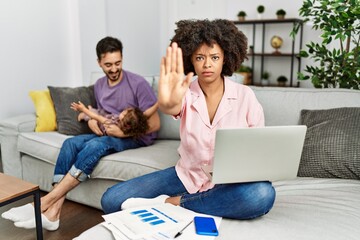 Mother of interracial family working using computer laptop at home doing stop sing with palm of the hand. warning expression with negative and serious gesture on the face.