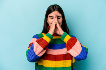 Young caucasian woman isolated on blue background holding hands in pray near mouth, feels confident.