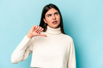 Young caucasian woman isolated on blue background showing a dislike gesture, thumbs down....