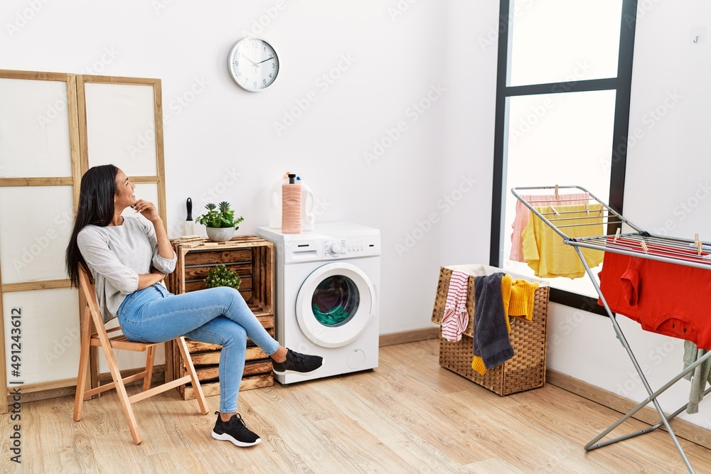 Wall mural Young latin woman bored waiting for washing machine at laundry room