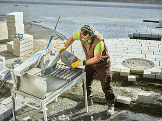 Construction worker holding paving stone by machinery for cutting at site